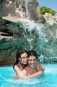 two-happy-swimmers-enjoy-a-custom-waterfall-pool-feature-with-rocks-on-sunny-day Two happy swimmers enjoy a custom waterfall pool feature with rocks on sunny day